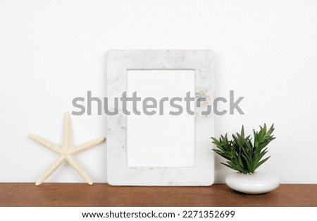 Mock up white marble frame with starfish and succulent plant on a shelf or desk. Wood shelf and white wall. Portrait frame orientation.