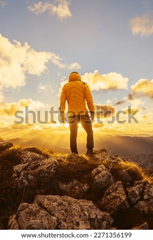 man alone on his back in a yellow jacket on a mountain peak contemplating the sunset in the backlight. Mountaineer contemplating the landscape after hiking in the mountains Royalty-Free Stock Photo #2271356199