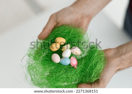Easter toys with green leaves in the hands of a man. Blurred background. Close up, copy space. Chicken eggs, twigs with green leaves on the hay. Easter holiday concept background.