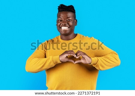 Smiling Young Black Man Showing Heart Gesture With Hands Near Chest, Happy Millennial African American Guy Making Love Sign At Camera While Posing Over Blue Studio Background, Copy Space