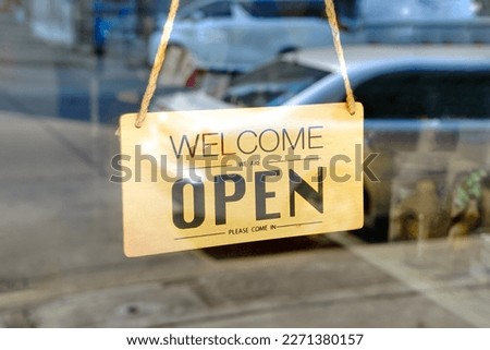 welcome we are open please come in sign on the glass door of the coffee shop.