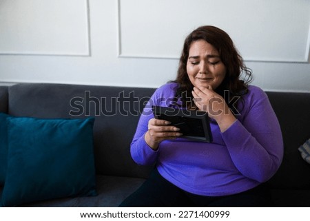 Heartbroken sad woman crying with smeared mascara and makeup missing her ex-boyfriend while looking at a photo frame