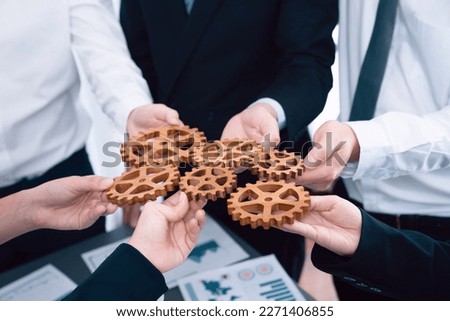 Closeup top view businesspeople hand holding gear and join together over meeting table with financial report papers. Cohesive group of office workers holding cog wheel as synergy harmony concept. Royalty-Free Stock Photo #2271406855