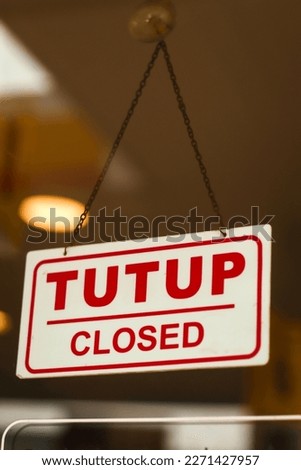 tutup (closed) sign on acrylic board hanging in front of a glass door at the entrance of the store with blurred lights background
