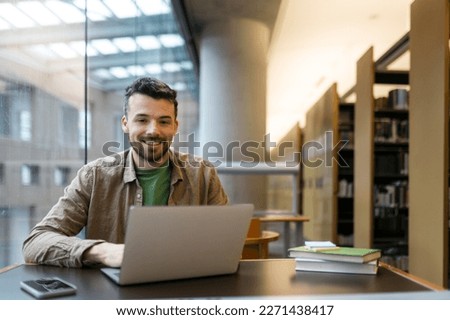 Portrait of smiling handsome hispanic businessman using laptop computer working freelance project  in modern office. Happy copywriter looking at camera sitting at workplace. Successful business  Royalty-Free Stock Photo #2271438417