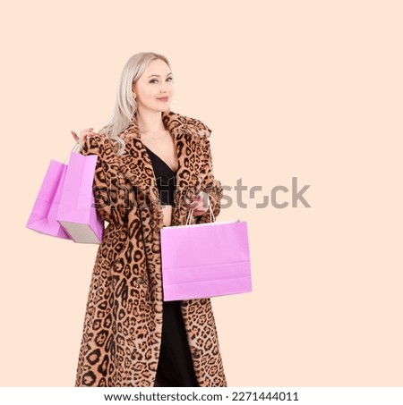 A blonde girl in a leopard-print faux fur coat holds shopping bags in her hands, isolated