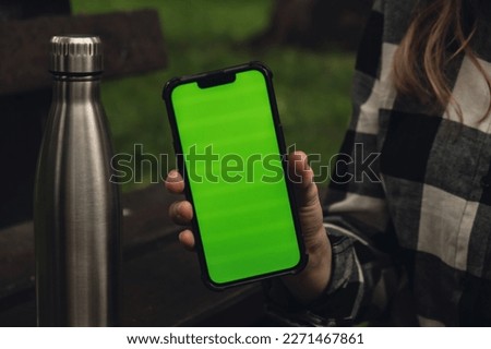 Mobile phone social media green screen Chroma key. Reusable steel thermo water bottle on wooden bench. Sustainable lifestyle. Plastic free zero waste free living. Go green Woman student work study