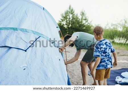 cute little caucasian boy helping father to put up a tent. sunset shadows from trees. Family camping concept. High quality photo