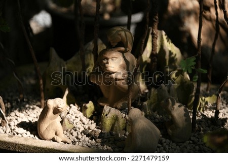Closeup tiny monkeys doll set of big papa monkey and small monkeys around him one on his head act like real monkey habits in the wild with rock and bonsai trees background .
