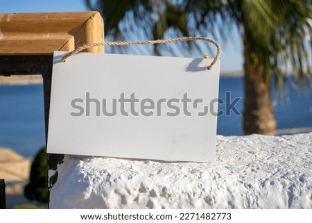 white painted wall with tropical blue sea in the background with white hanging picture sign with empty free space for template or blank copy area 