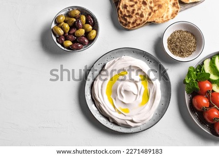 Labneh yogurt cream cheese with olive oil, zaatar, olives, vegetables and pita bread on white table, copy space. Traditional arabian or middle eastern breakfast with labneh dip. arabic cuisine.