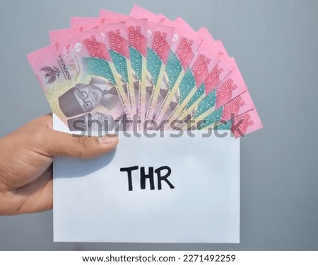 Indonesian Money, rupiah or IDR in envelope with THR Text. Hand holding THR envelope. THR is holiday allowance on Eid al-Fitr or Lebaran days. background white best quality. Royalty-Free Stock Photo #2271492259