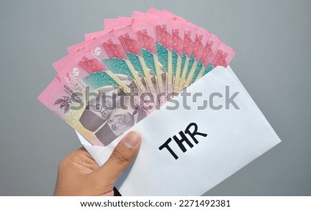 Indonesian Money, rupiah or IDR in envelope with THR Text. Hand holding THR envelope. THR is holiday allowance on Eid al-Fitr or Lebaran days. background white best quality. Royalty-Free Stock Photo #2271492381