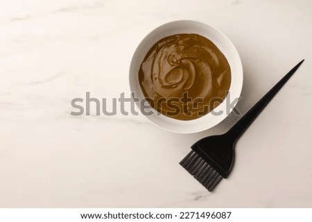 Bowl of henna cream and brush on white marble table, flat lay with space for text. Natural hair coloring