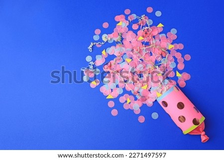 Colorful confetti and streamers bursting out of party cracker on blue background, flat lay. Space for text