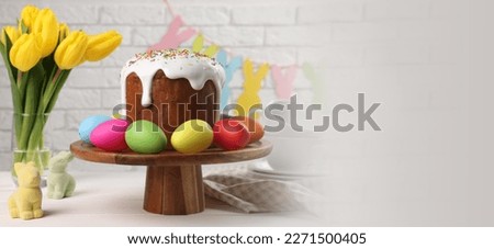Stand with tasty Easter cake and decorated eggs on white wooden table, space for text. Banner design