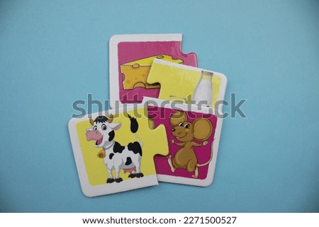 Educational puzzle pieces with pictures of cheese, milk, cow and mouse mixed up on a blue background.