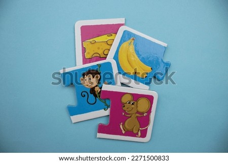 Educational puzzle pieces with pictures of cheese, banana, monkey and mouse mixed up on a blue background.