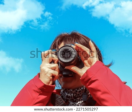 Woman photographer taking pictures through digital camera against blue sky