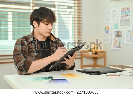 Image of focused asian male using digital tablet, working on mobile application software design project at workstation