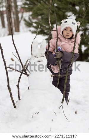 Funny Winter games in the snowy park, little cute asian girl made a snowman in the form of a hare, winter lifestyle photo