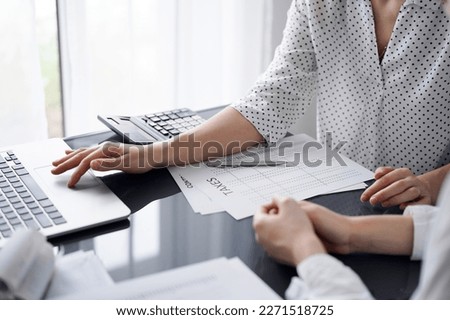 Woman accountant using a calculator and laptop computer while counting taxes for a client. Business audit and finance concepts.