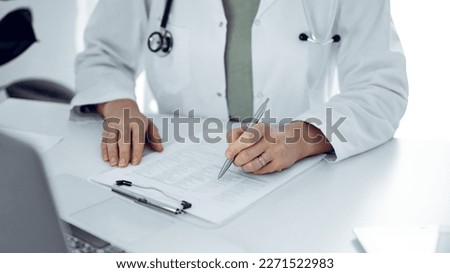 Unknown doctor woman sitting and writing notes at the desk in clinic or hospital office, close up. Medicine concept.
