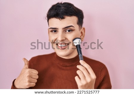 Non binary person applying make up smiling happy and positive, thumb up doing excellent and approval sign 