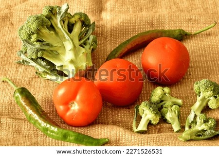 The picture shows a still life composed of ripe cauliflower vegetables, red tomatoes and a few hot chili peppers.