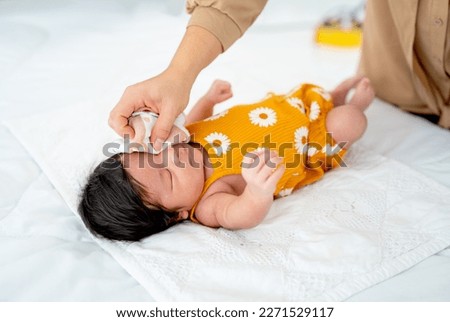 Close up mother hand use towel to clean in area of eye and face of newborn baby lie on bed with day light.