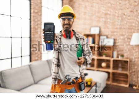 Young hispanic man worker smiling confident holding data phone with credit card at home