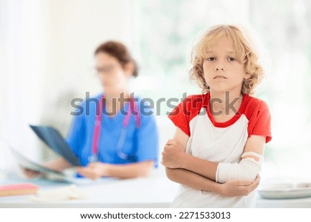 Child with arm injury at trauma and emergency care. Kid with elbow cast at health clinic. Doctor checking x-ray of injured little boy. Kids hospital.  Royalty-Free Stock Photo #2271533013