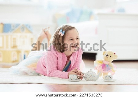 Little girl playing with doll house in white sunny bedroom. Kid with toys. Role game for young children. Child with teddy bear toy. Kids play tea party with stuffed animals and dolls. Nursery interior Royalty-Free Stock Photo #2271533273