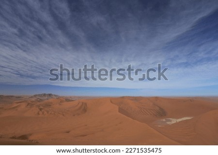 desert landscape with white clay pan and red sand dunes under partly cloudy blue sky