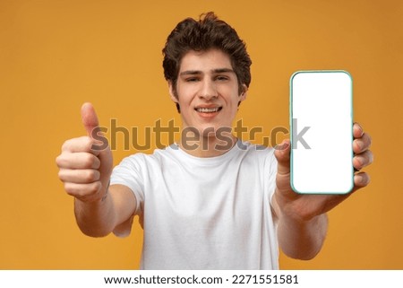Smiling young man showing mobile phone blank white screen mockup to camera.