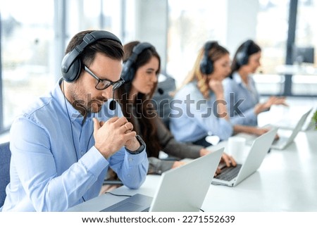 Pensive male customer service operator listening to customer over headset and thinking about appropriate solutions for client issues at call center. Helpdesk worker team concept. Royalty-Free Stock Photo #2271552639