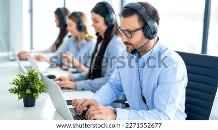 Call center operator agents in headset communicating with clients at online support service office. Serious man wearing hands-free headset using laptop. Royalty-Free Stock Photo #2271552677