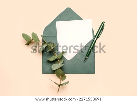 Envelope with blank card, pen and eucalyptus branch on color background