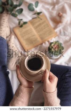 Concept for wishing a good spring morning. A girl with a cup of espresso in her hands and a book lying on the bed surrounded by young greenery. Spring flat lay. Selective focus. Royalty-Free Stock Photo #2271557979