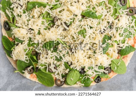Italian cuisine raw thin pizza with fresh spinach, olives and cheese. Close-up on a board on a table. horizontal top view from above