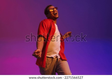 Young cheerful african guy wearing sunglasses dancing isolated over purple neon studio background