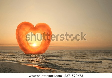 Picturesque sunset at sea. Sun going down, view through gap in heart formed from clouds