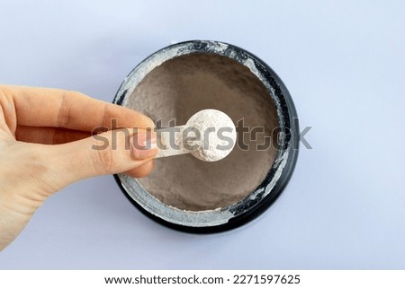 Black jar with electrolytes in measuring spoon in woman's hand on white background, top view