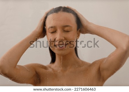 Young woman under trickles water in pleasure shower. Beautiful girl under spray of water on isolated background. Wet happy face