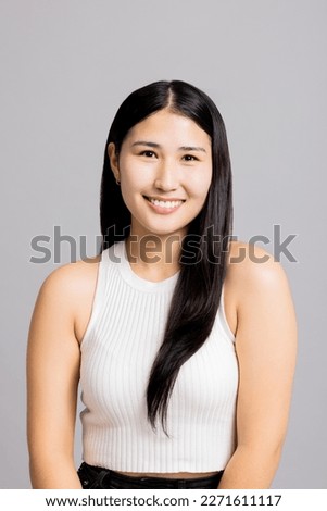 Portrait of happy delighted young asian woman girl in basic clothes sitting on grey background in studio isolated looking at camera smiling in good mood.