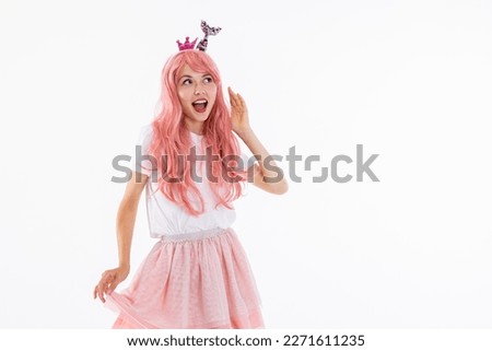 Delighted young girl in pink wig looking at camera deightfully wearing white t-shirt and pink skirt standing on white background in studio isolated posing showing different emootions. Royalty-Free Stock Photo #2271611235