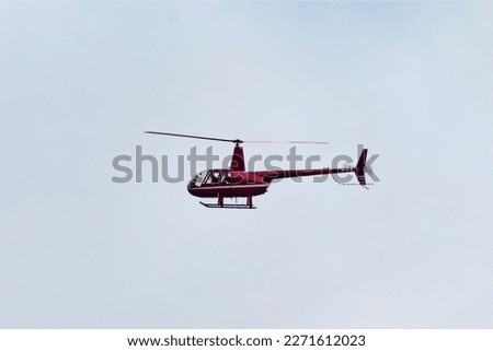 A small red helicopter flying in the sky