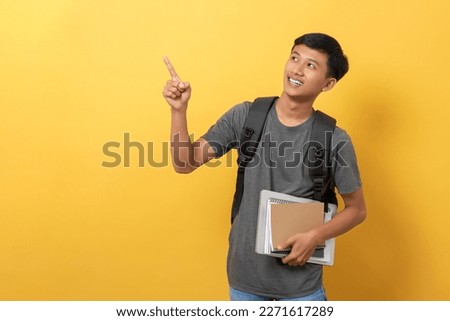 Smiling young college student with books and backpack isolated on yellow background pointing with fingers to the side present a product