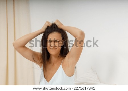Attractive girl headache, it's time to get up for work. Beautiful young woman, dressed in silk negligee of delicate blue color, is sitting in cozy bed in the bedroom, holding her head.