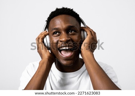Portrait of happy delighted excited african american black guy model student posing over grey background in studio isolated singing listening to music while posing for shooting process.
